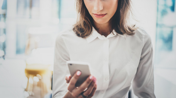 Frau mit weißer Bluse schaut auf Smartphone