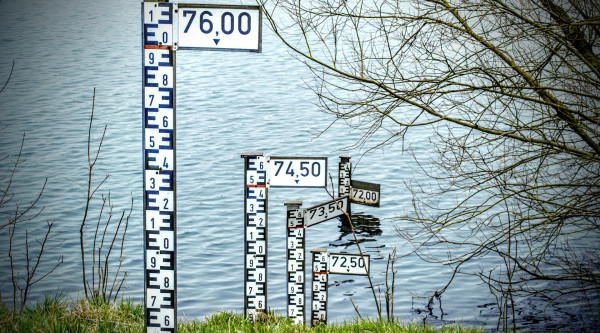 An der Böschung eines Flusses stehen in Abständen Markierungen für Hochwasser. 