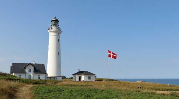 Ein Leuchtturm vor blauem Himmel. Ein dänische Flagge weht im Wind. 
