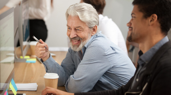 Generationenmanagemnt Offboarding: Ein älterer und ein jüngerer Mitarbeiter sitzen zusammen entspannt vor einem Rechner