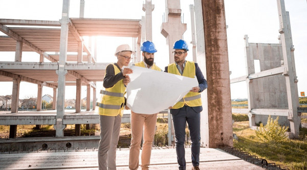 Drei Architekten mit Bauplan auf einer Baustelle