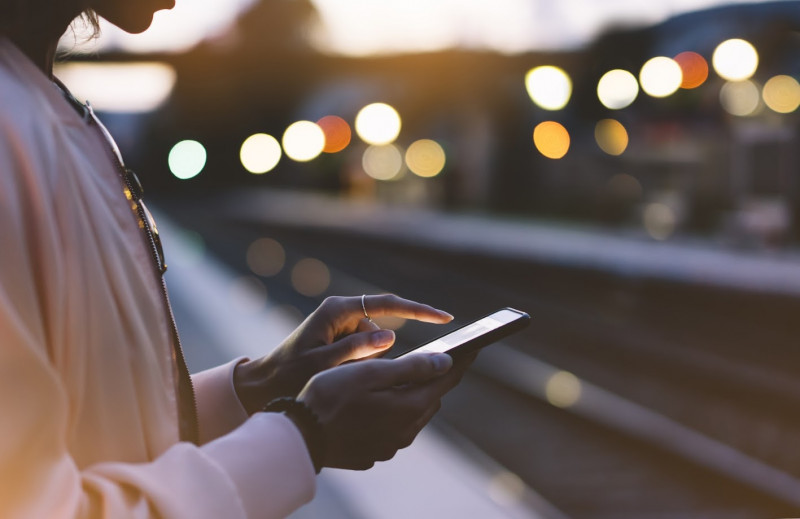 Eine Frau steht in einem Bahnhof und tippt auf ihr Handy