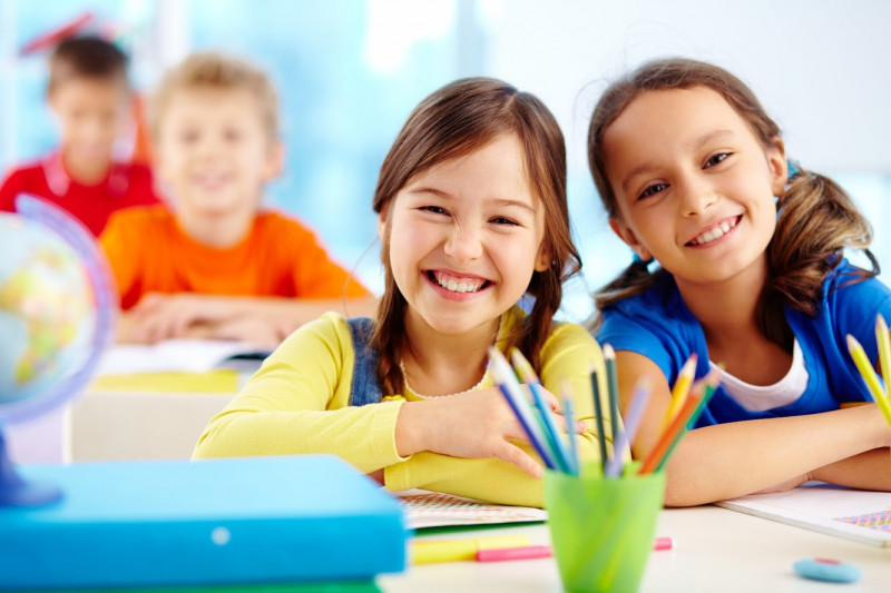 Lachende Kinder sitzen an einem Tisch, vor sich Papier und Malstifte