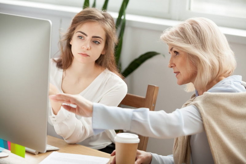 Senior- und junge weibliche Kollegen diskutieren Online-Projekt. Blick auf PC-Bildschirm