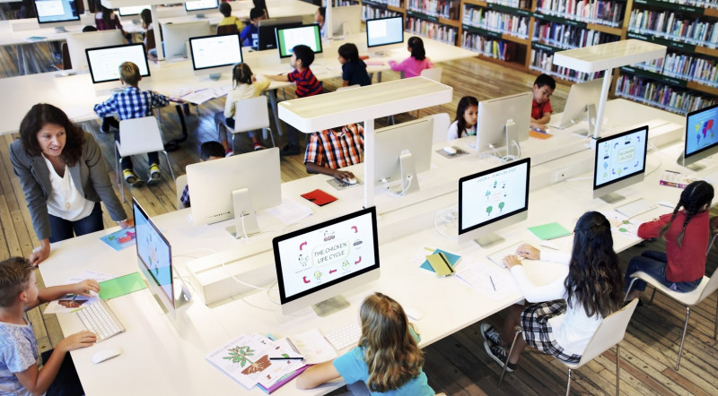 Kinder sitzen in einem Schulraum vor Computer-Bildschirmen