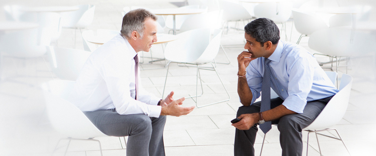 Zwei Männer in Hemd und Krawatte sitzen sich gegenüber und diskutieren