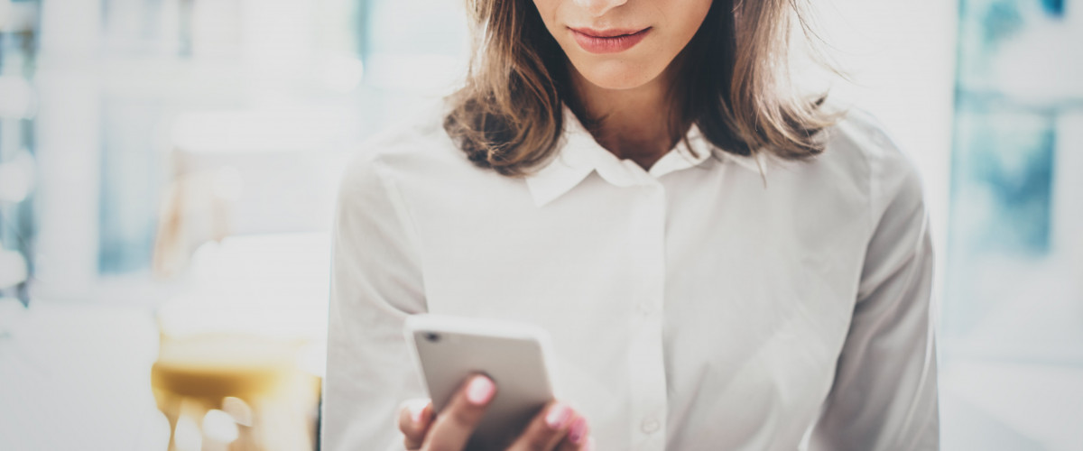 Frau mit weißer Bluse schaut auf Smartphone