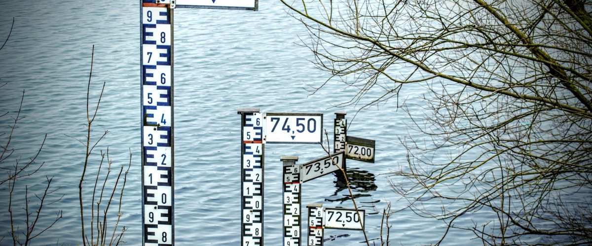 Interaktive Hochwasserkarten An der Böschung eines Flusses stehen in Abständen Markierungen für Hochwasser.