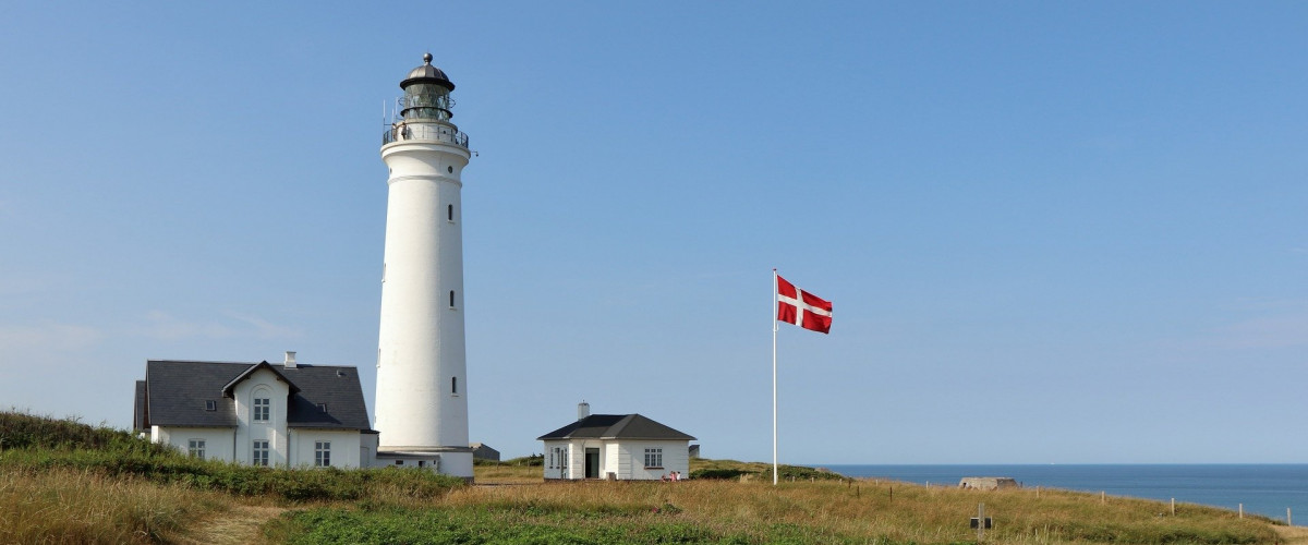 Ein Leuchtturm vor blauem Himmel. Ein dänische Flagge weht im Wind. 