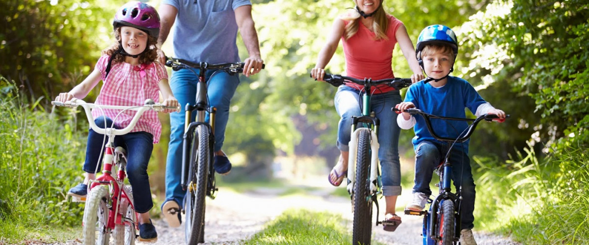 Mutter, Vater und zwei Kinder fahren Fahrrad auf einem Waldweg