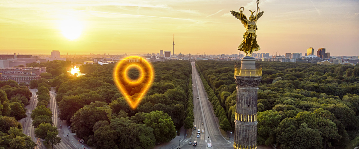 Ein Geo-Pin markiert einen Punkt auf einem Foto vom Berliner Tiergarten und der Siegessäule