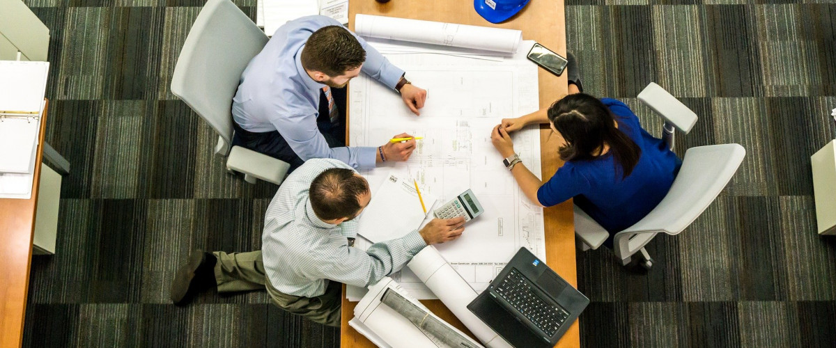 Trends im Projektmanagement Drei Geschäftsleute sitzen über Papiere gebeugt an einem Tisch