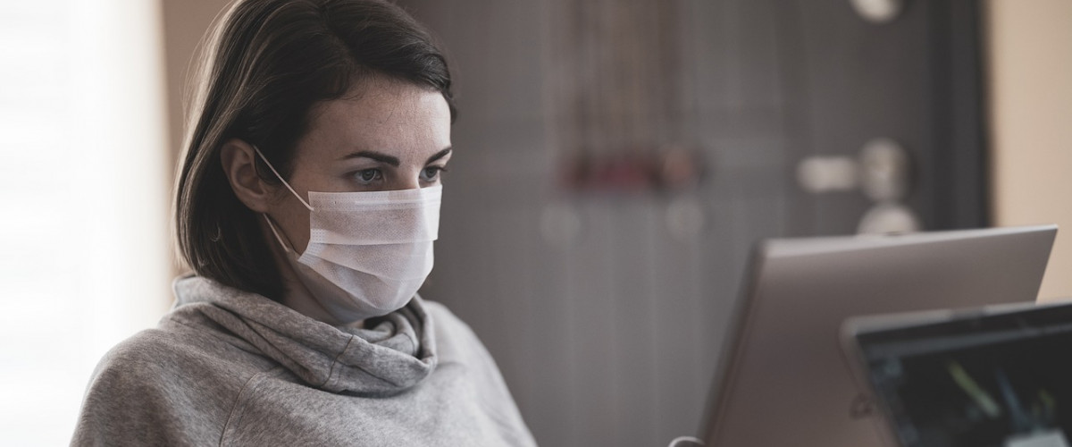 Eine Mitarbeiterin sitzt mit Mundschutz vor einem Bildschirm
