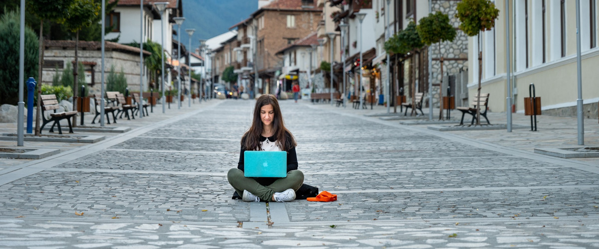 Eine Frau sitzt auf der Straße und tippt in ein Laptop